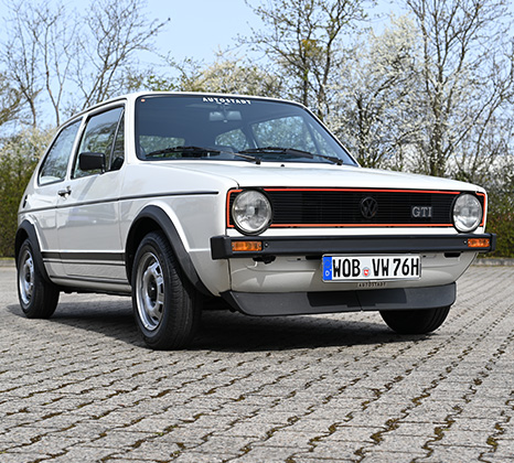 Ein weißer VW Golf 1 GTI im Dreiviertelprofil auf einer gepflasterten Straße.